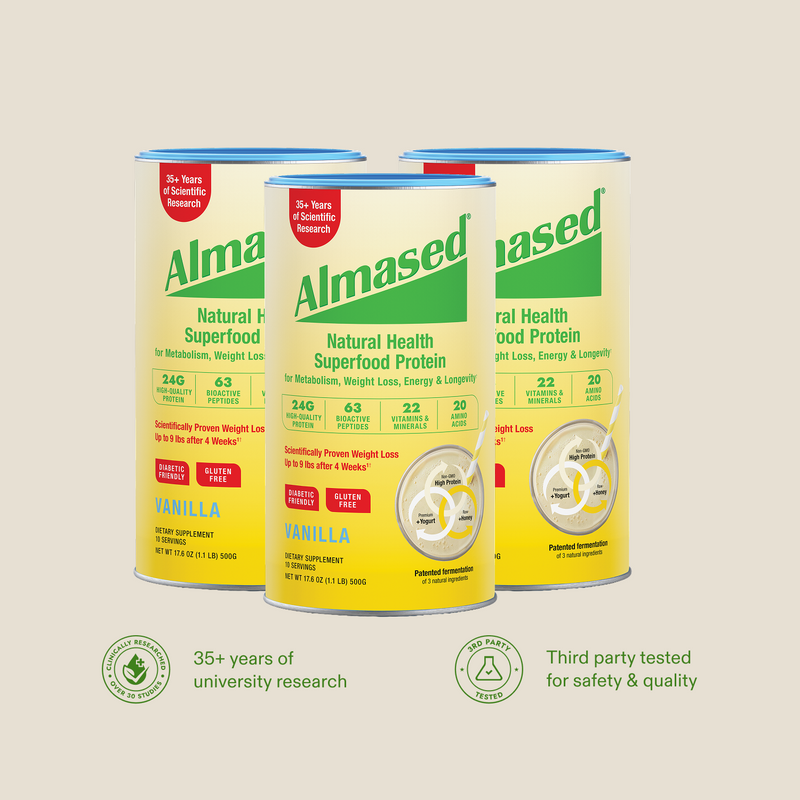 Three cans of Almased Natural Health Superfood Protein powder in Vanilla flavor, arranged on a light beige background with green circular trust badges below.