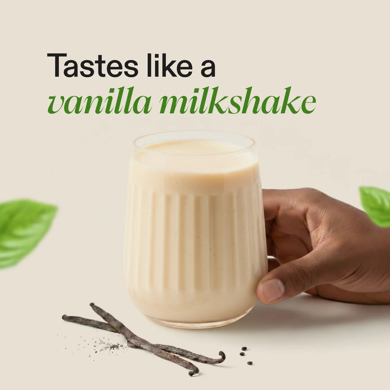 A hand holds a ribbed glass of creamy vanilla milkshake against a light beige background, with the text 'Tastes like a vanilla milkshake' above it and vanilla beans and leaves as props.